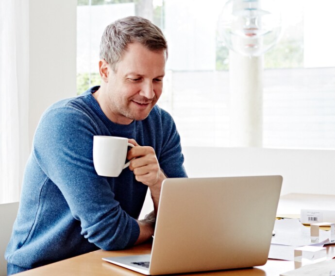 Homme à la maison utilisant un ordinateur portable et buvant du café.